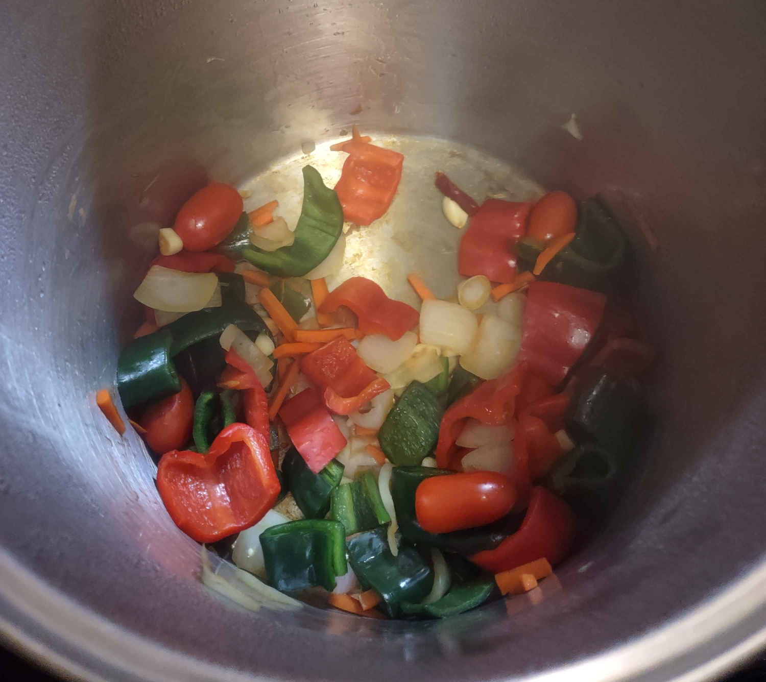 photo of a pot containing two poblano, one jalapeno, and two arbol chilis, a la rogue red pepper, half a sweet onion, a carrot, five sweet grape tomatoes, and half a head of garlic. the pan is just started to get a glaze from cooking